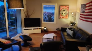 A living room with a television, a couch, a coffee table, and a window with a view of trees.