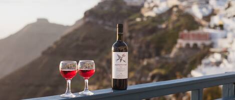 A wine bottle and two glasses on a balcony with a view of a mountainous town.