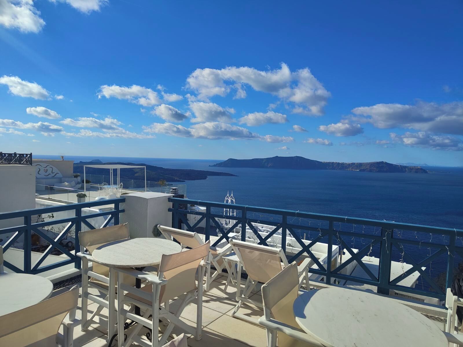 A terrace with outdoor seating overlooking a body of water and distant landforms.