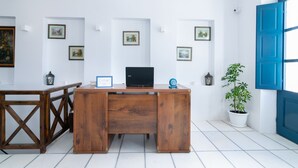 Ein Schreibtisch aus Holz mit einem Laptop, umgeben von gerahmten Bildern an der Wand, einer Topfpflanze und einer blauen Tür.