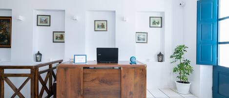 A wooden desk with a laptop, surrounded by framed pictures on the wall, a potted plant, and a blue door.