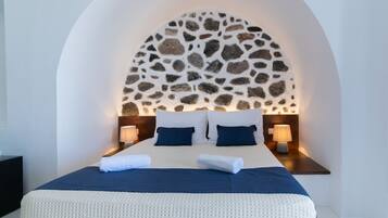 A hotel room with a large bed, white walls, a stone wall arch, and two bedside lamps.