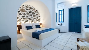 Ein modernes Hotelzimmer mit einem großen Bett, einem Bogen aus Stein, einer blauen Tür und einem weißen Fliesenboden.