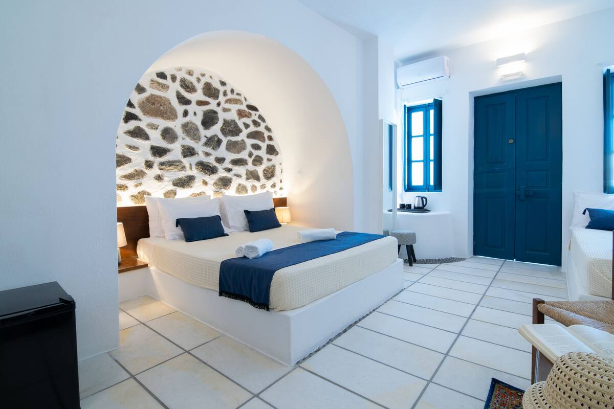Ein modernes Hotelzimmer mit einem großen Bett, einem Bogen aus Stein, einer blauen Tür und einem weißen Fliesenboden.