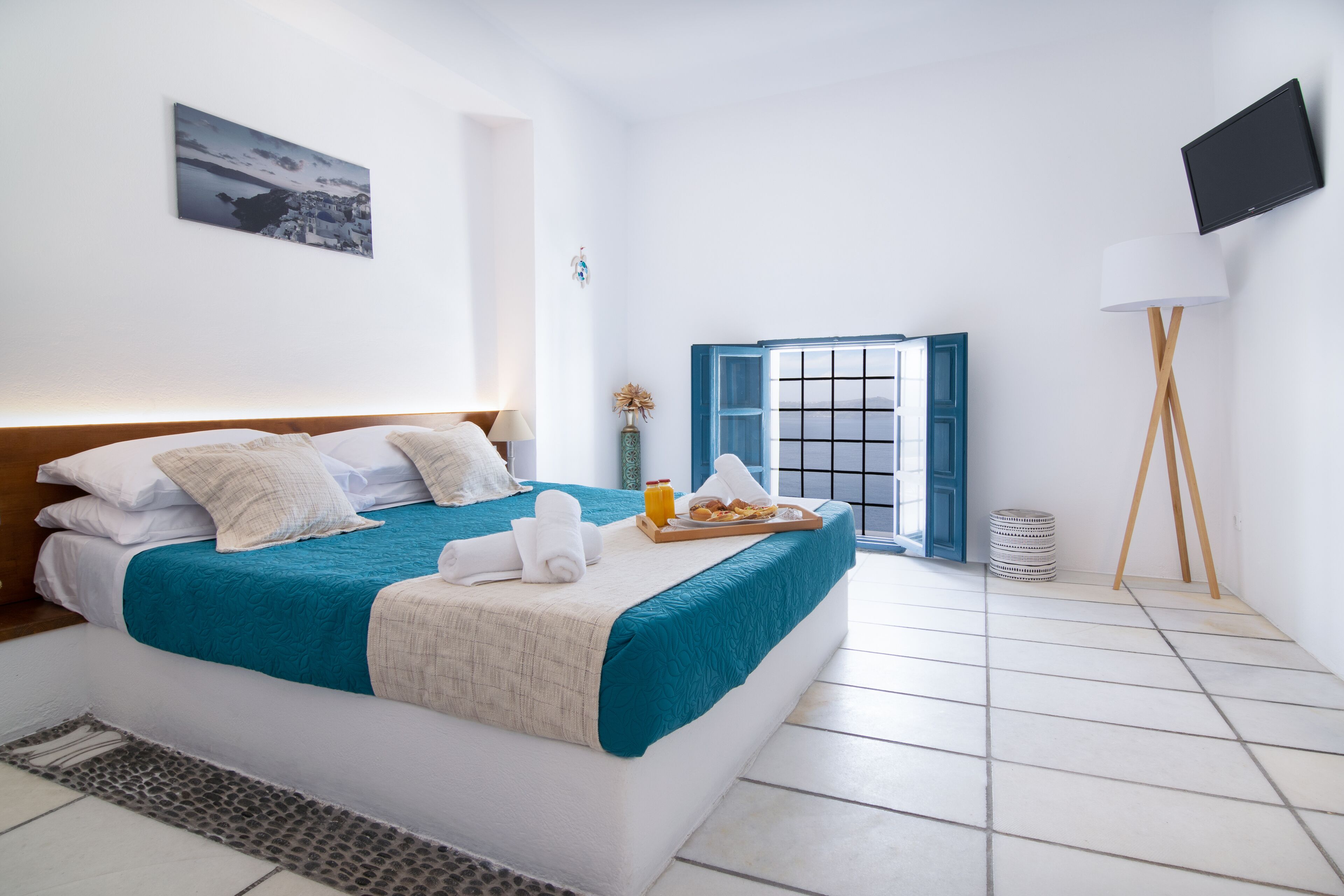 A neatly made bed with a blue and white bedspread, a tray with breakfast items, and a view of the sea through an open door.