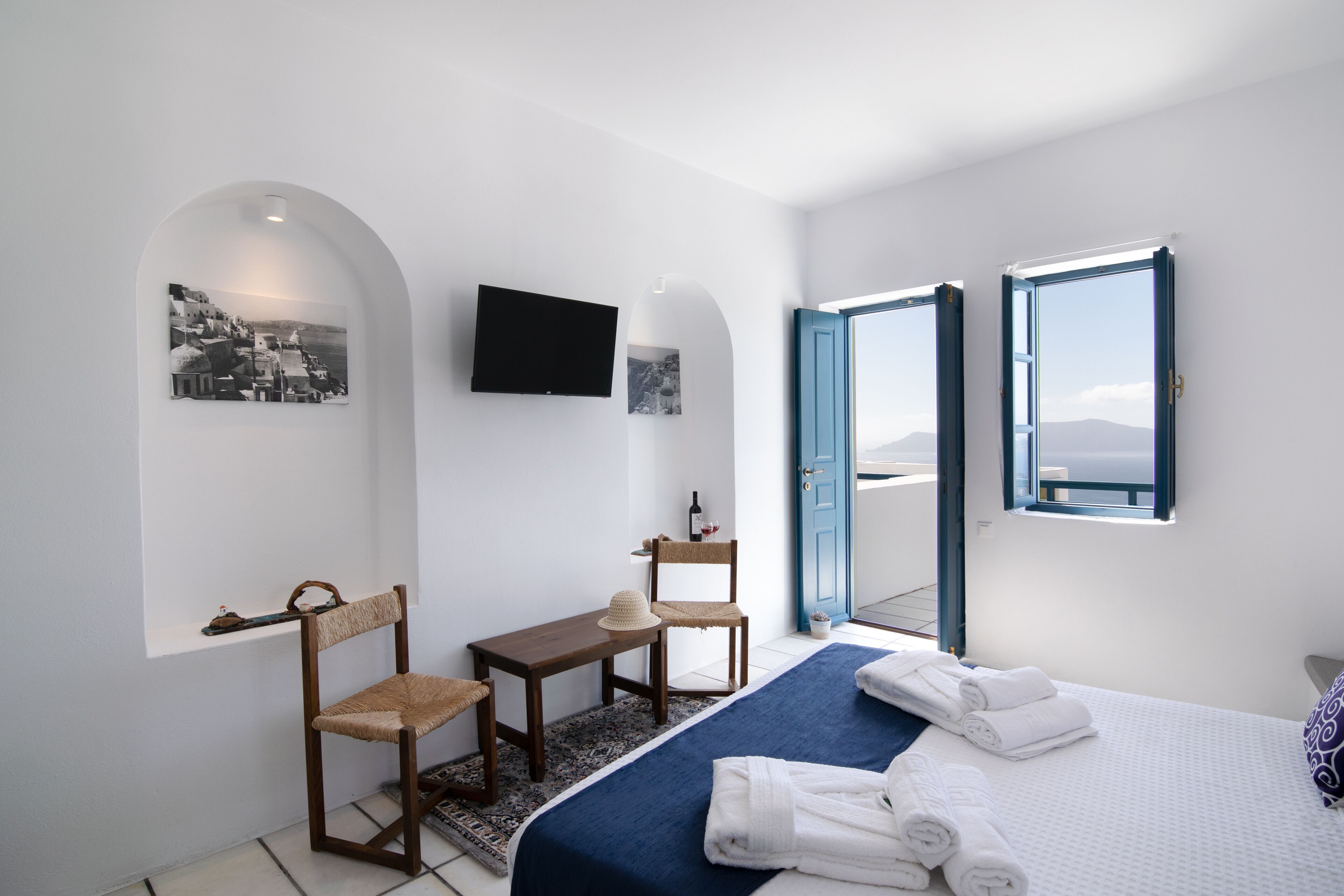 A hotel room with a bed, a desk, a chair, a television, and a view of the sea through a door.