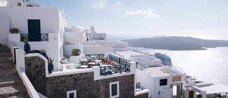 A white building with a stone facade, a staircase, and a view of the sea.