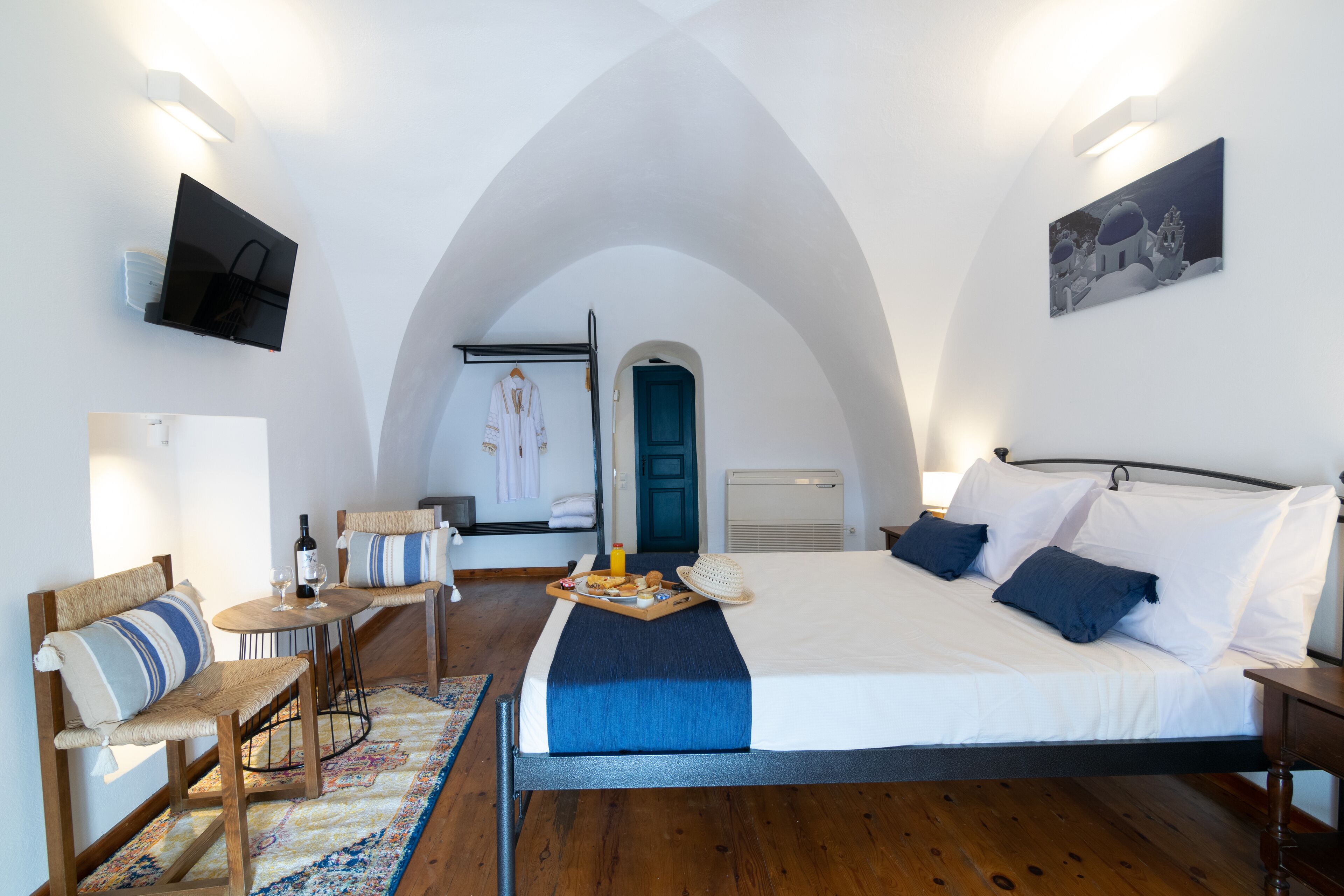 Un dormitorio con una cama grande, un escritorio y una silla. Hay un cuadro en la pared y un televisor montado allí.