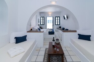 Habitación de hotel moderna con decoración blanca, un sofá, una mesita con una botella y vasos, y vistas a través de un arco.