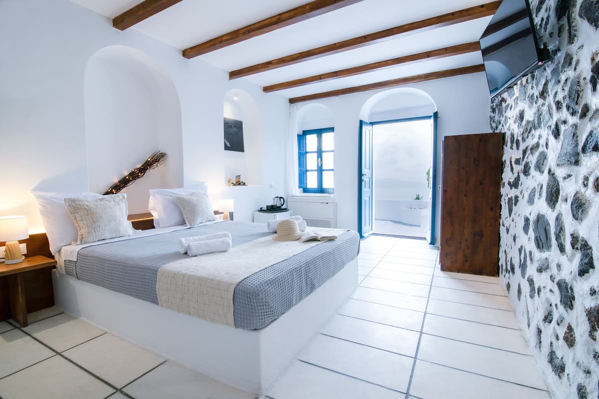 Ein Schlafzimmer mit einem großen Bett, Holzbalken, weißen Wänden, einer Steinwand und Blick ins Freie.