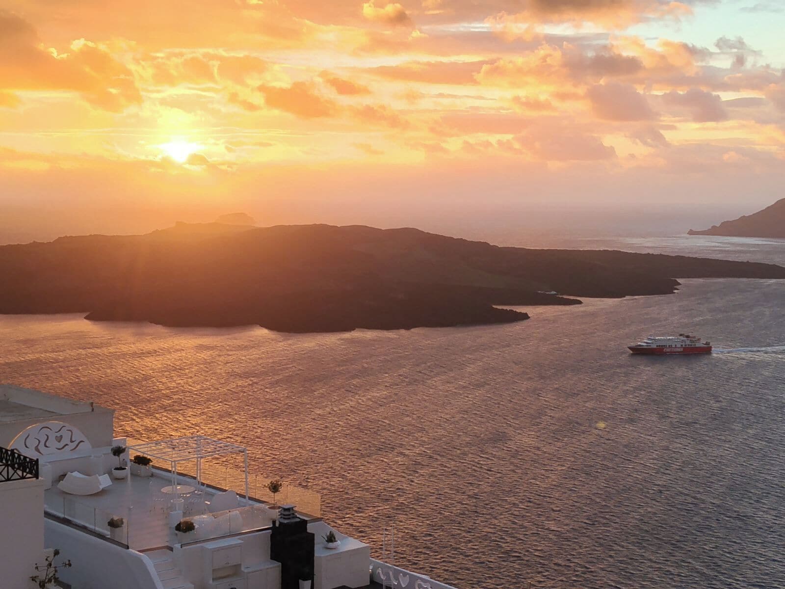 Vista costera con atardecer, un barco en el agua y un edificio con terraza.