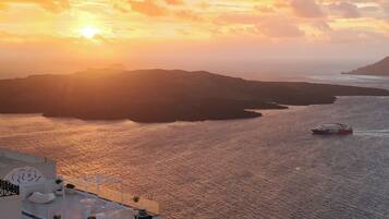 A coastal view with a sunset, a boat on the water, and a building with outdoor seating.
