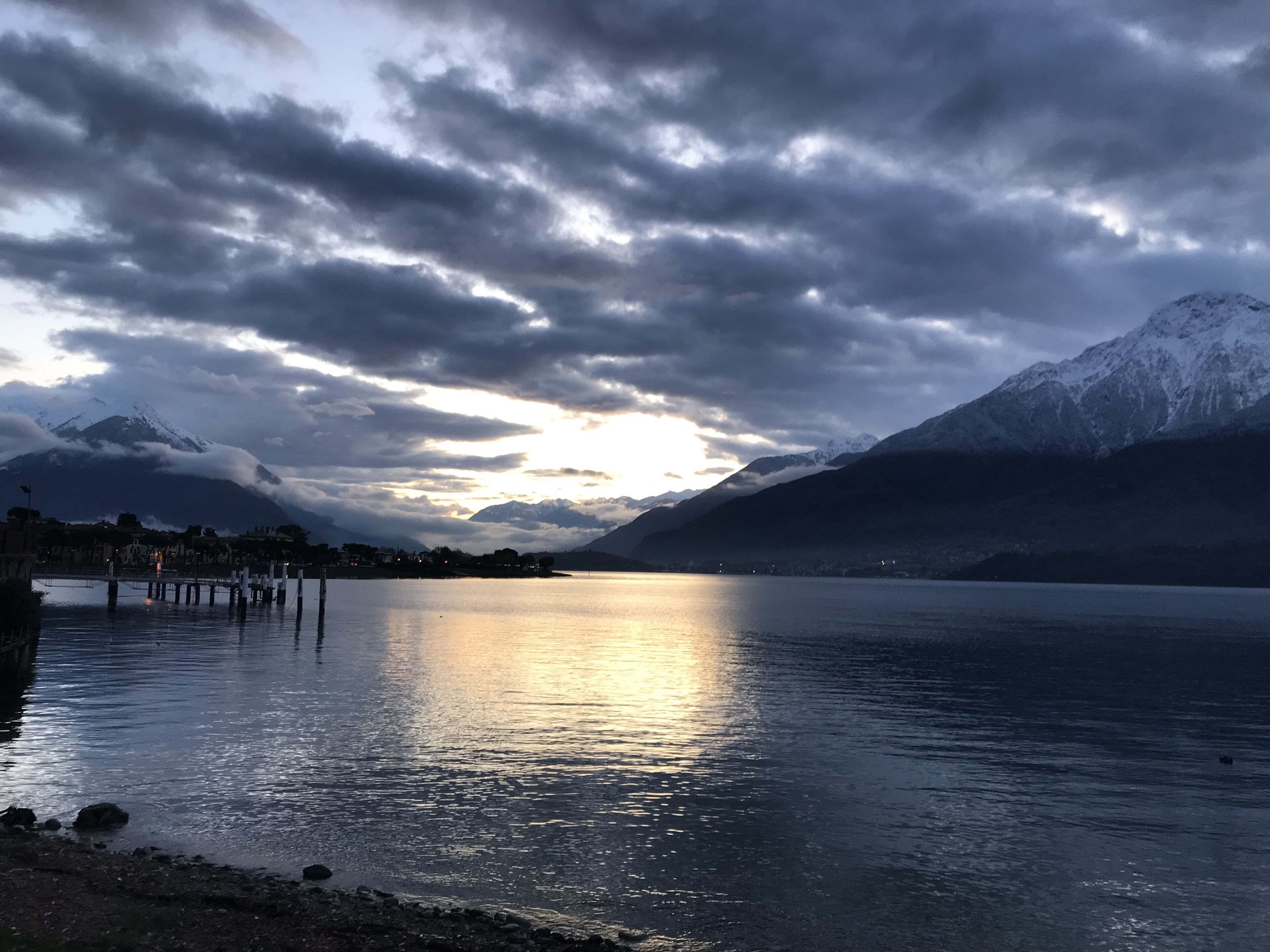 A calm lake with mountains in the background and a cloudy sky.