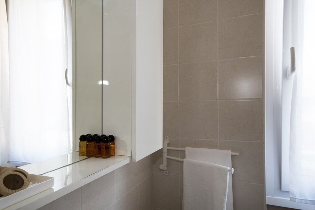 A bathroom with a glass shelf holding toiletries, a towel rack, and a window with curtains.