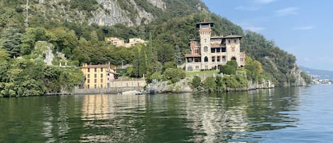 A large, historic building with multiple stories and a tower, situated on a hillside overlooking a calm lake.