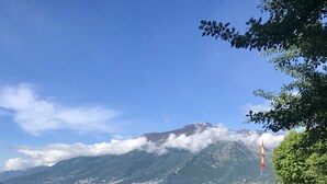 A lakeside view with a mountain in the background, a flag, and boats on the water. - Lakeside Apartment with a swimming pool, free parking, and free Wi-Fi (Domaso)