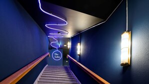 Un escalier avec des rampes en bois et un panneau néon indiquant «
The Lucho
», dans un couloir aux murs bleu foncé et doté d’un luminaire.