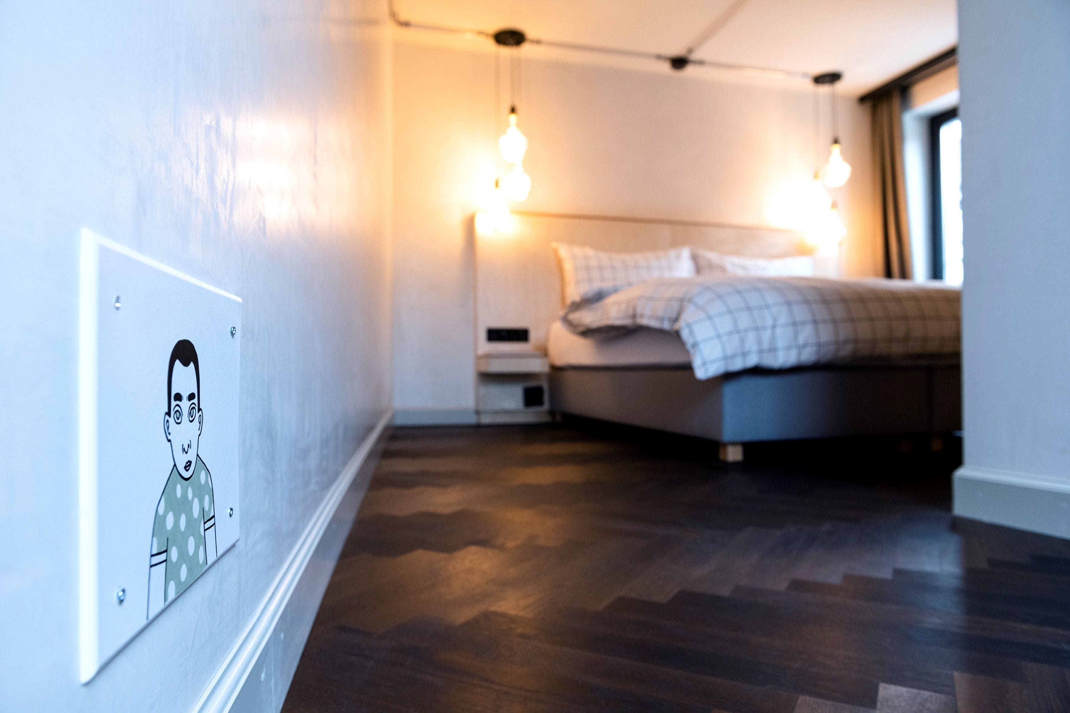 A modern hotel room with a wooden floor, a bed with a checkered duvet, and two bedside lamps.