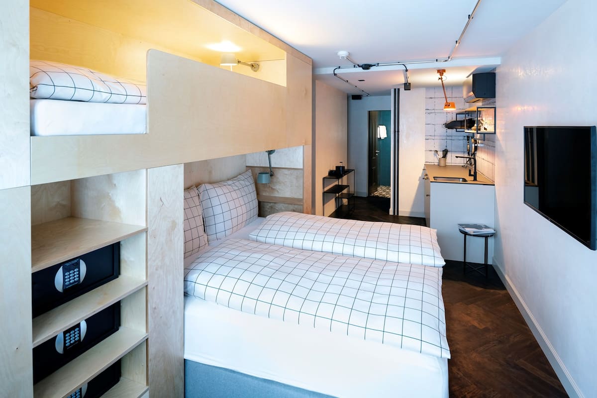 A compact bedroom with a bunk bed, a small kitchenette, and a bathroom visible through an open door.