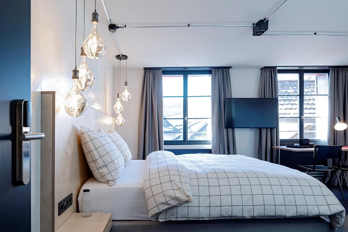 A modern hotel room with a bed, a desk, and a TV.