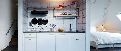 A compact kitchen with white cabinets, a black range hood, and a red pendant light.