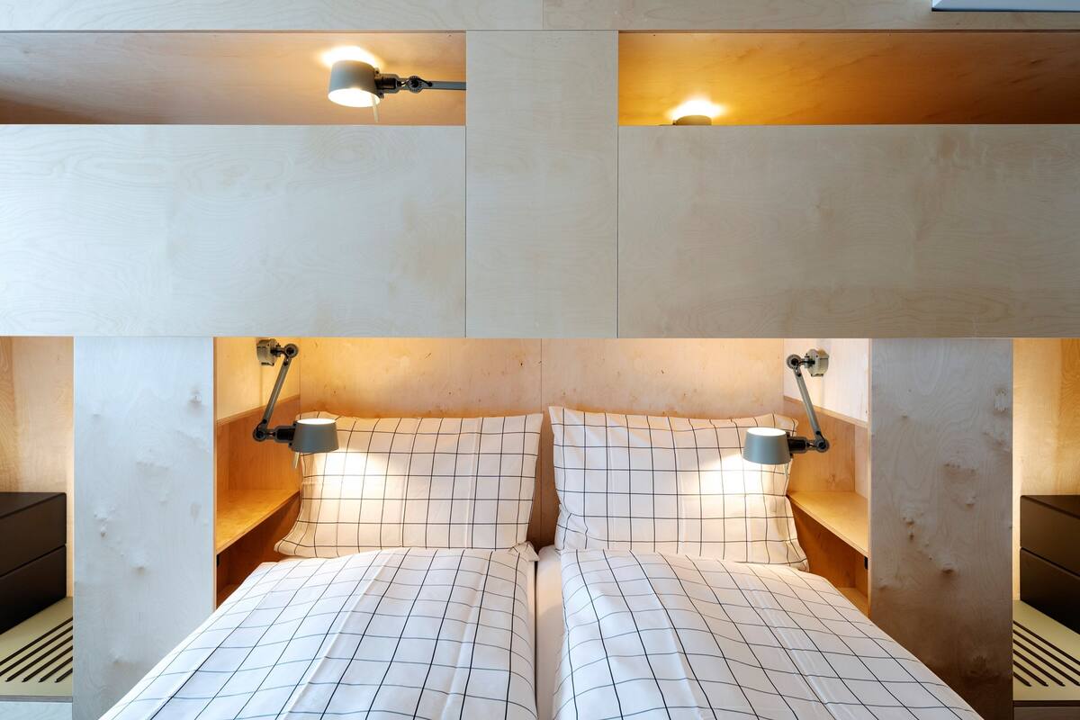 A double bed with a grid-patterned bedspread, two bedside lamps, and a wall-mounted light fixture above the bed.