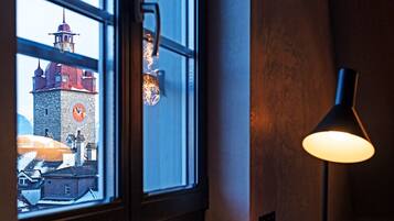 Une pièce faiblement éclairée, avec une fenêtre donnant sur un beffroi, un bureau avec une lampe et un plateau contenant une théière et des tasses.