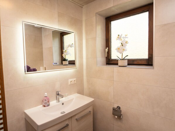 A bathroom with a large mirror, a sink, a window with an orchid, and a towel rack.