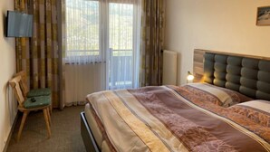 A hotel room with a bed, a chair, a television, and a window with curtains.