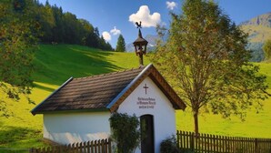 A small church with a cross on the front, surrounded by a wooden fence and a tree.