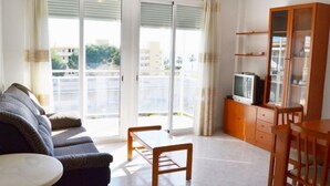 Un salón con sofá, una mesa de centro, un televisor sobre un mueble de madera y un ventanal corredero que da a un balcón.