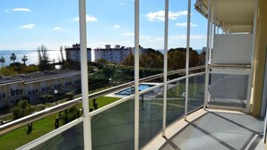 Un balcón con vistas despejadas a una piscina, un área verde y edificios al fondo.