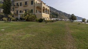 A large, yellow building with multiple floors and arched windows, surrounded by a grassy area and palm trees. - Bella Vista by Interhome (Ventimiglia)