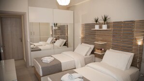A modern hotel room with two beds, a large mirror, a wooden slatted headboard, and a small shelf with plants.