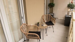 A balcony with wicker chairs and a small table, a potted plant, and a view of the building's exterior.