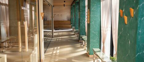 A spa area with a glass wall, wooden benches, and a green marble wall.