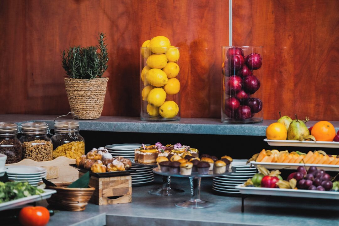 A buffet table with various food items, including fruits, pastries, and a potted plant.