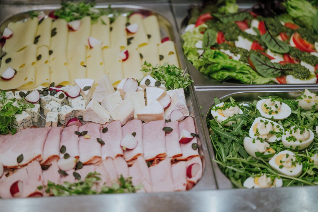 A buffet with various food options including sliced meats, cheeses, and salads.