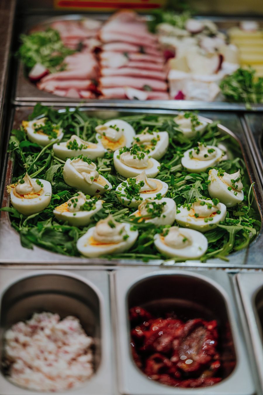 Un bufé con diversas opciones de comida, incluyendo carnes en rodajas, una ensalada con lonchas de huevo y dos acompañamientos.