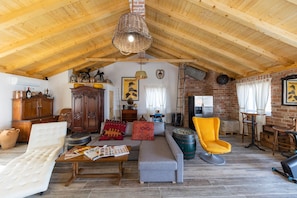 A rustic loft with exposed wooden beams, a loft bed, a sofa, a yellow armchair, and a dining area with a brick wall and wooden table. - Villa Maza (Pasman)