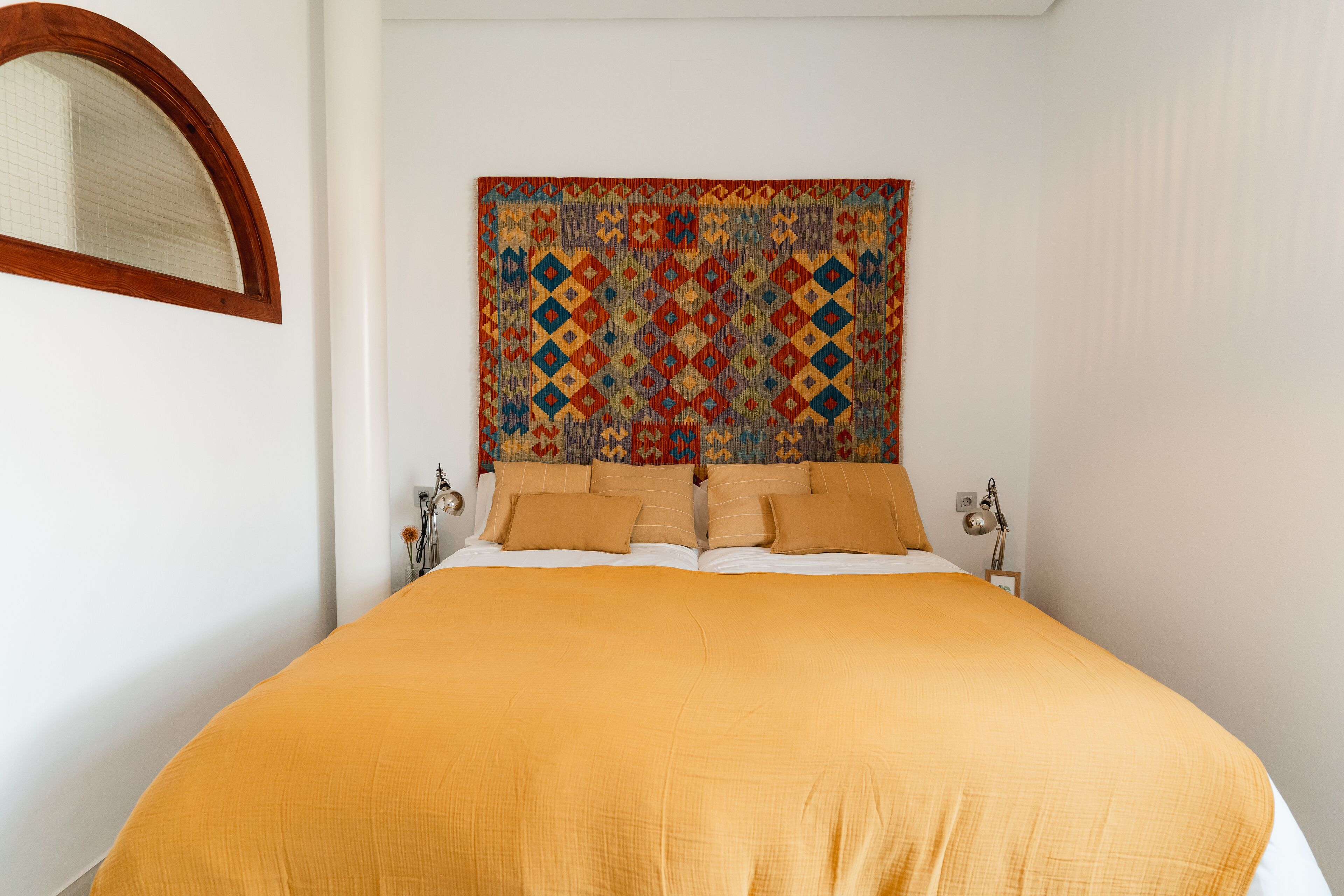 Un lit bien fait, avec une tête de lit à motifs, une lampe de chevet et un miroir au mur.
