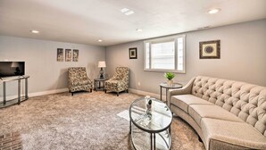 Un salon avec un canapé beige, deux fauteuils à motifs, une table basse en verre et un téléviseur posé sur un meuble.