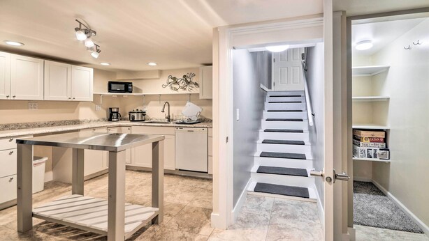 Une cuisine moderne avec des meubles blancs, une table en acier inoxydable et un escalier menant à une chambre à coucher située en mezzanine.