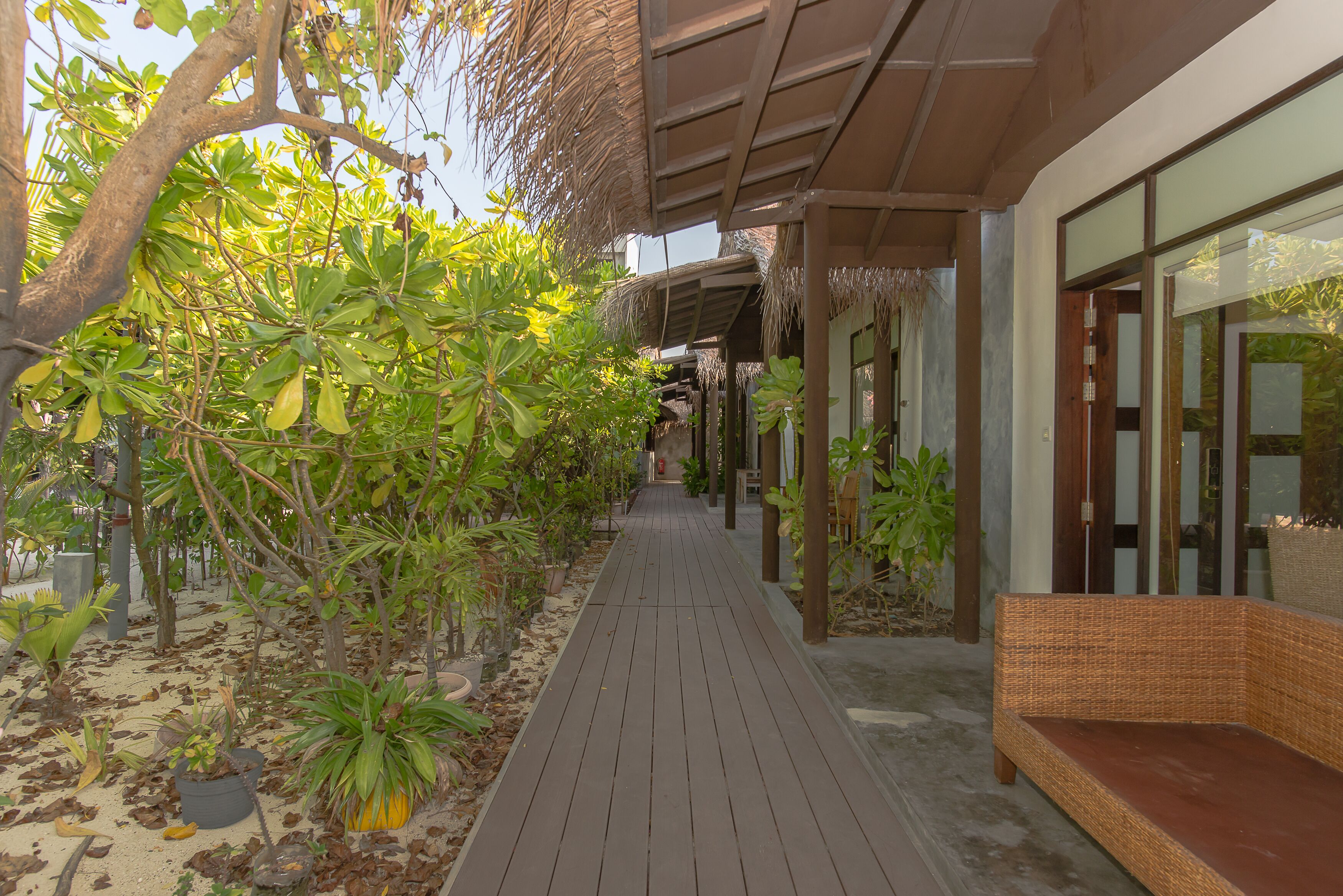 A wooden pathway leading to a building with a covered area and a wicker bench.