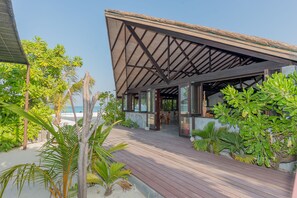 Un resort frente a la playa con terraza de madera, asientos al aire libre y plantas tropicales.