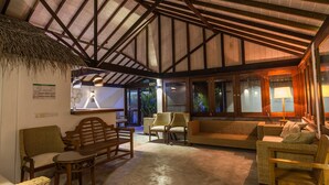 A cozy lounge area with wicker furniture, a thatched roof, and a view of the outdoors. - Premier Beach (Gulhi)