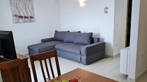A living room with a sofa, a dining table with a fruit bowl, and a TV. - Apartments Mlikota (Nin)