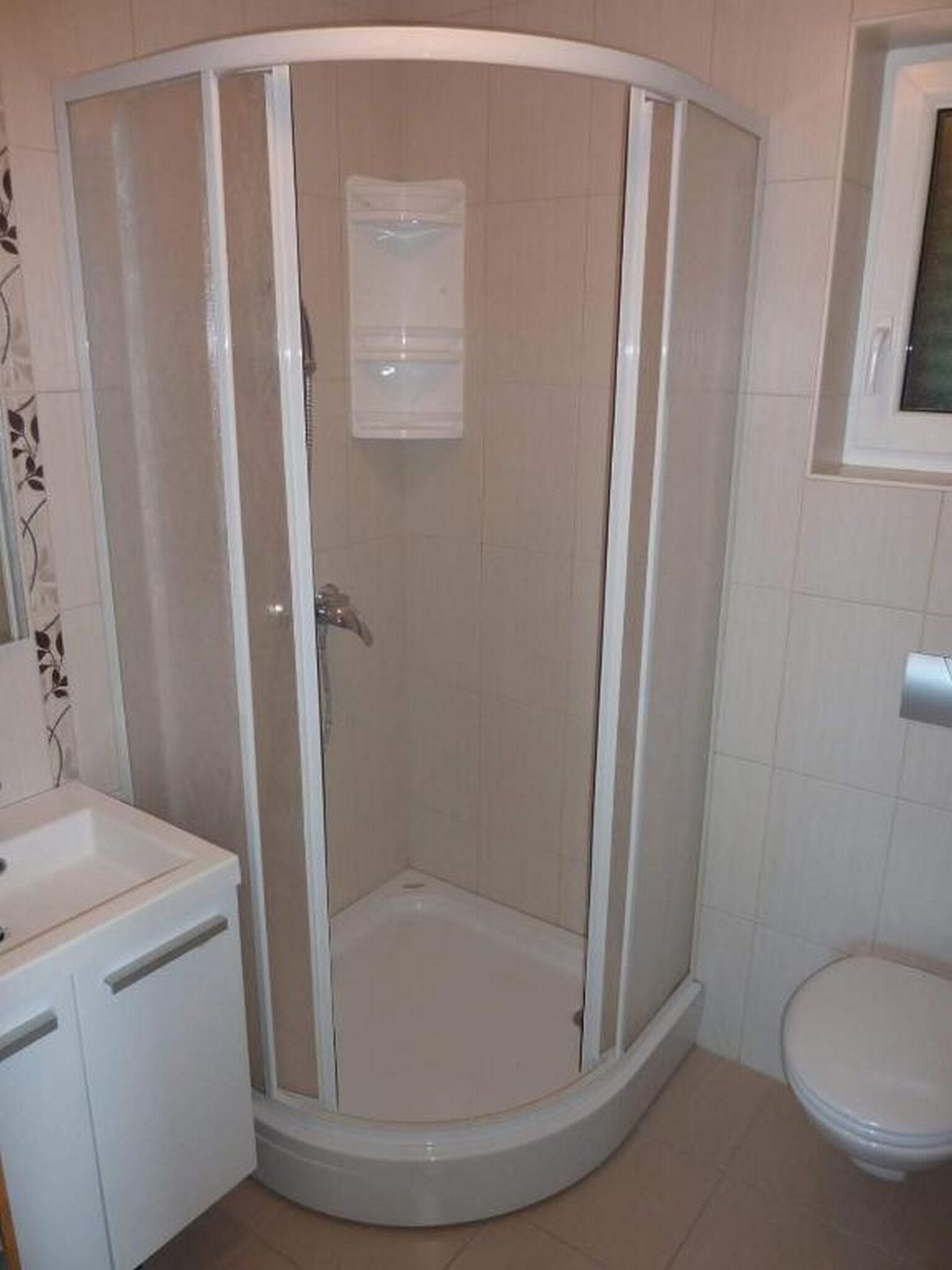 A corner bathroom with a glass-enclosed shower, a toilet, and a sink.