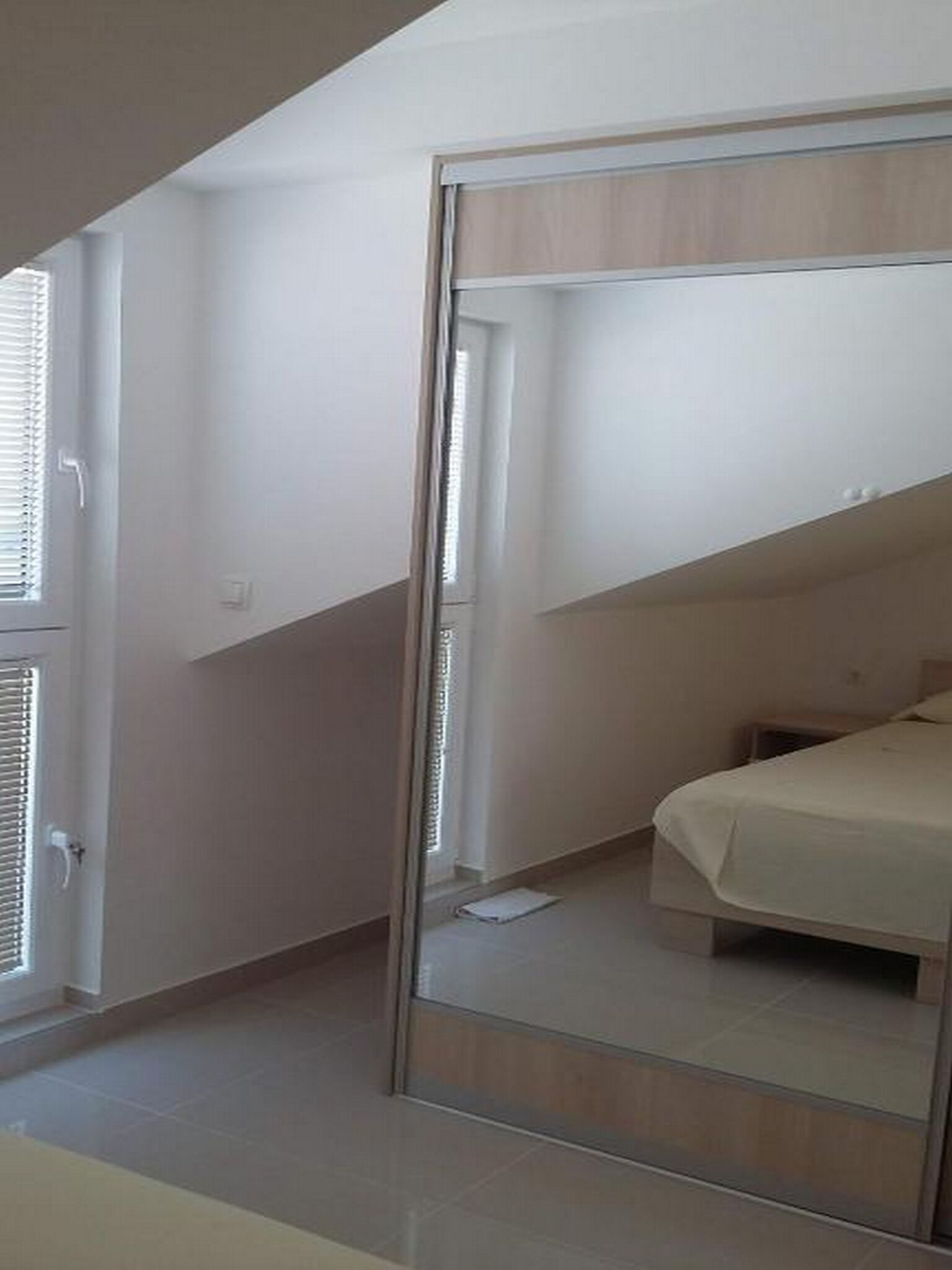 A bedroom with a bed, a wardrobe, and a window with blinds.
