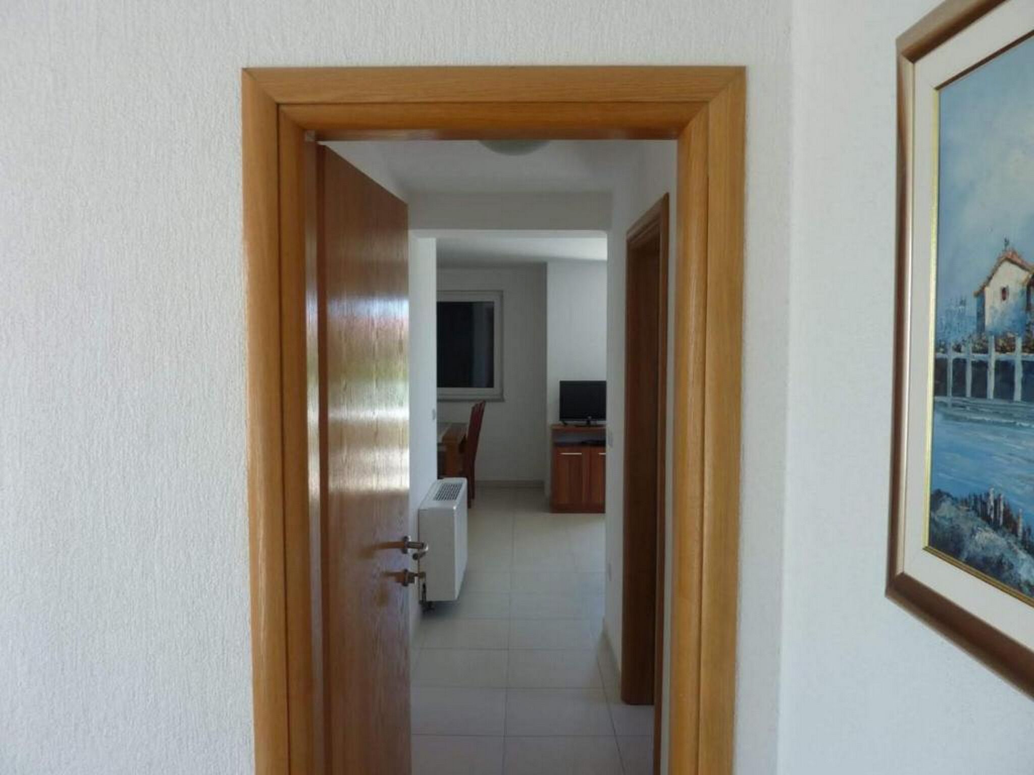Un couloir menant à une chambre équipée d’une télévision et d’un bureau.
